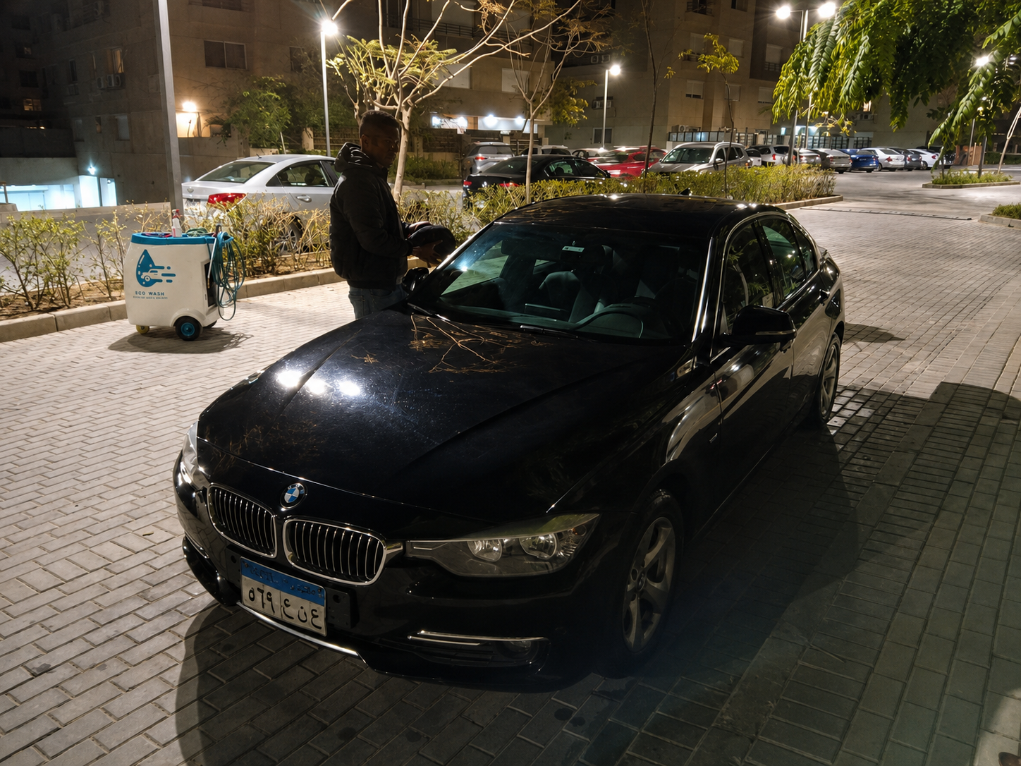 Equa Wash cart and worker beside a BMW 3 Series at night in a residential compound